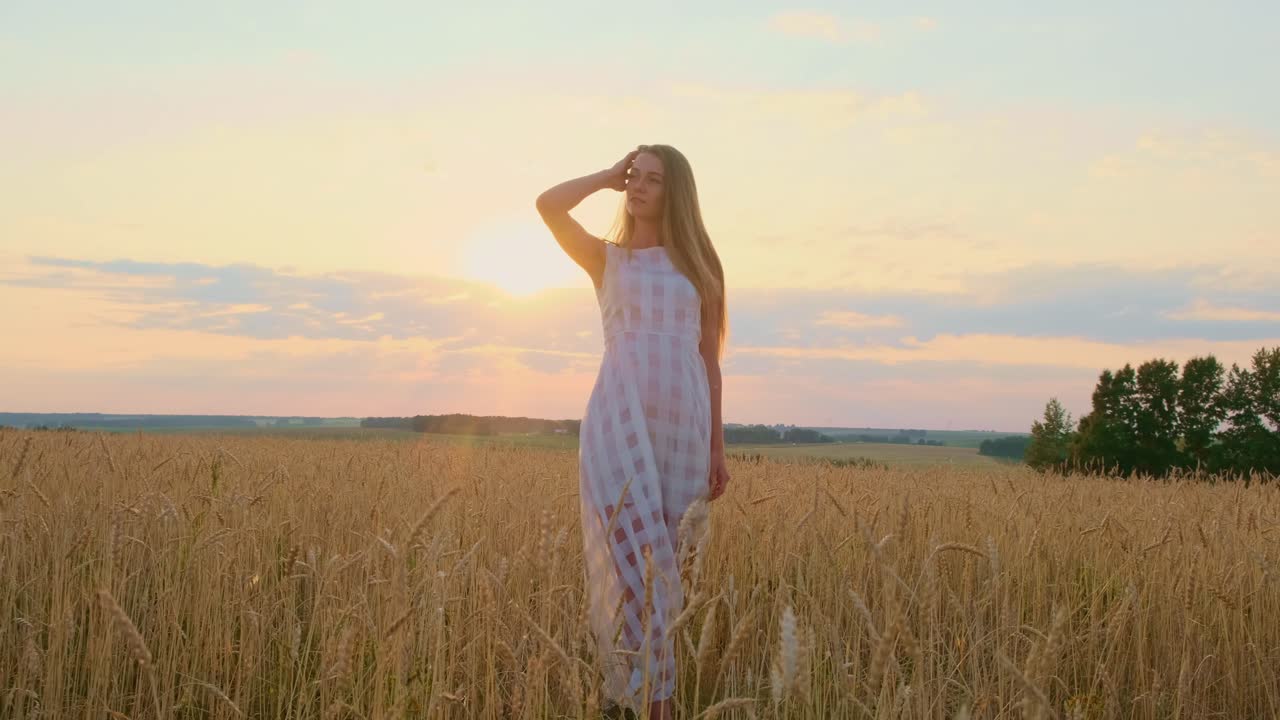 Woman in white dress walking through a wheat field at sunset