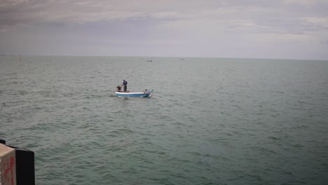 vista costa afuera de un pescador de pie en un pequeño barco de pesca por el muelle de hua hin en el golfo de tailandia