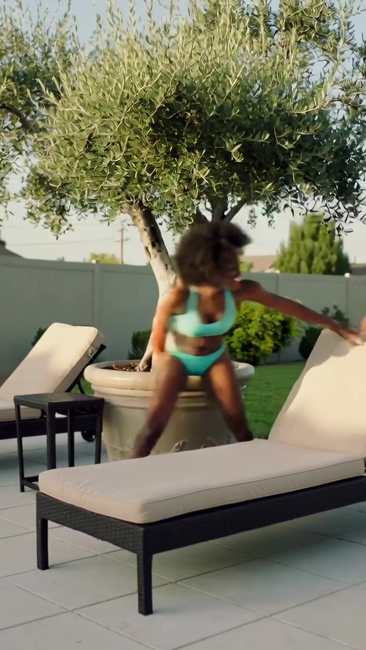 Vertical video: Running man in white tank starting chase across pool patio woman passing planter