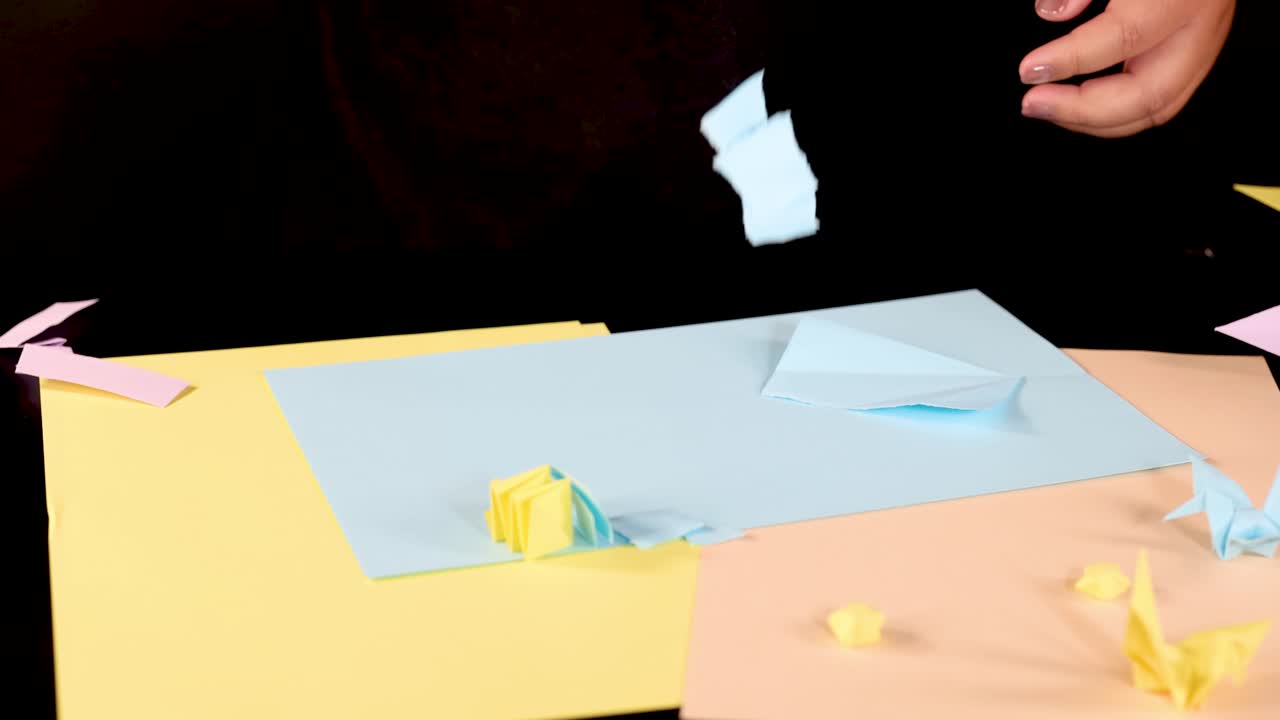 Person tears blue paper by hand on colorful craft table, studio lighting, static overhead shot