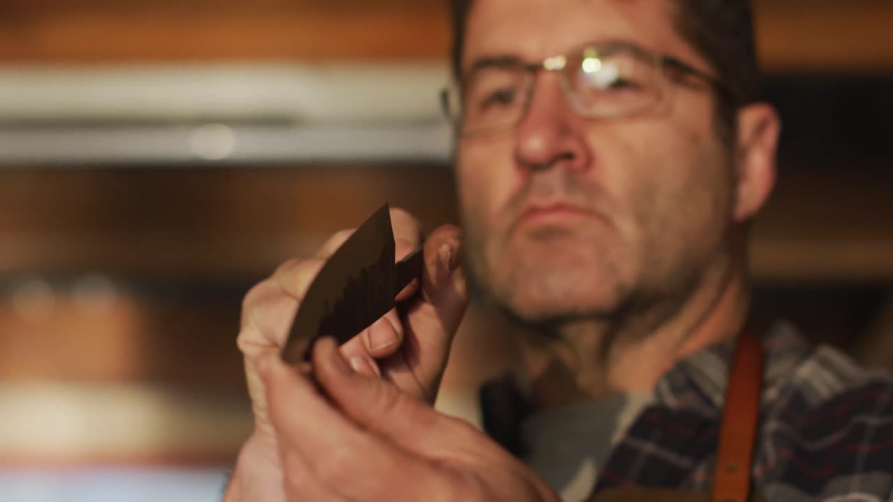 primer plano de un hombre caucásico fabricante de cuchillos en un taller, sosteniendo y comprobando un cuchillo