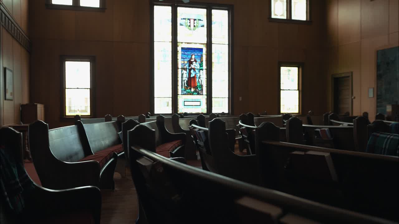 Cinematic view of an empty church interior, featuring soft light, wooden details, and a stained-glass window of Jesus with sheep