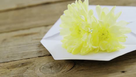 gelbe blumen in einem umschlag auf einer holzplatte