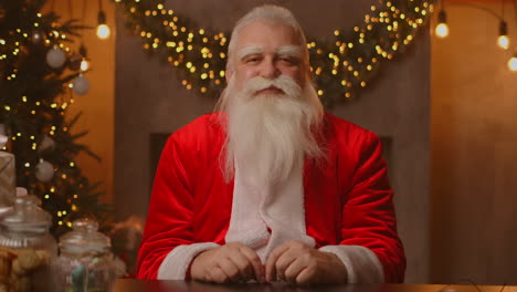 babbo natale è seduto a un tavolo in un bellissimo soggiorno decorato per un felice natale. babbo natali ha sorriso e ha annuito in accordo. filmati 4k di alta qualità