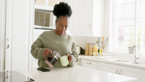 Feliz-Mujer-Mayor-Afroamericana-Sirviendo-Café-Y-Sonriendo-En-Una-Cocina-Soleada,-Cámara-Lenta