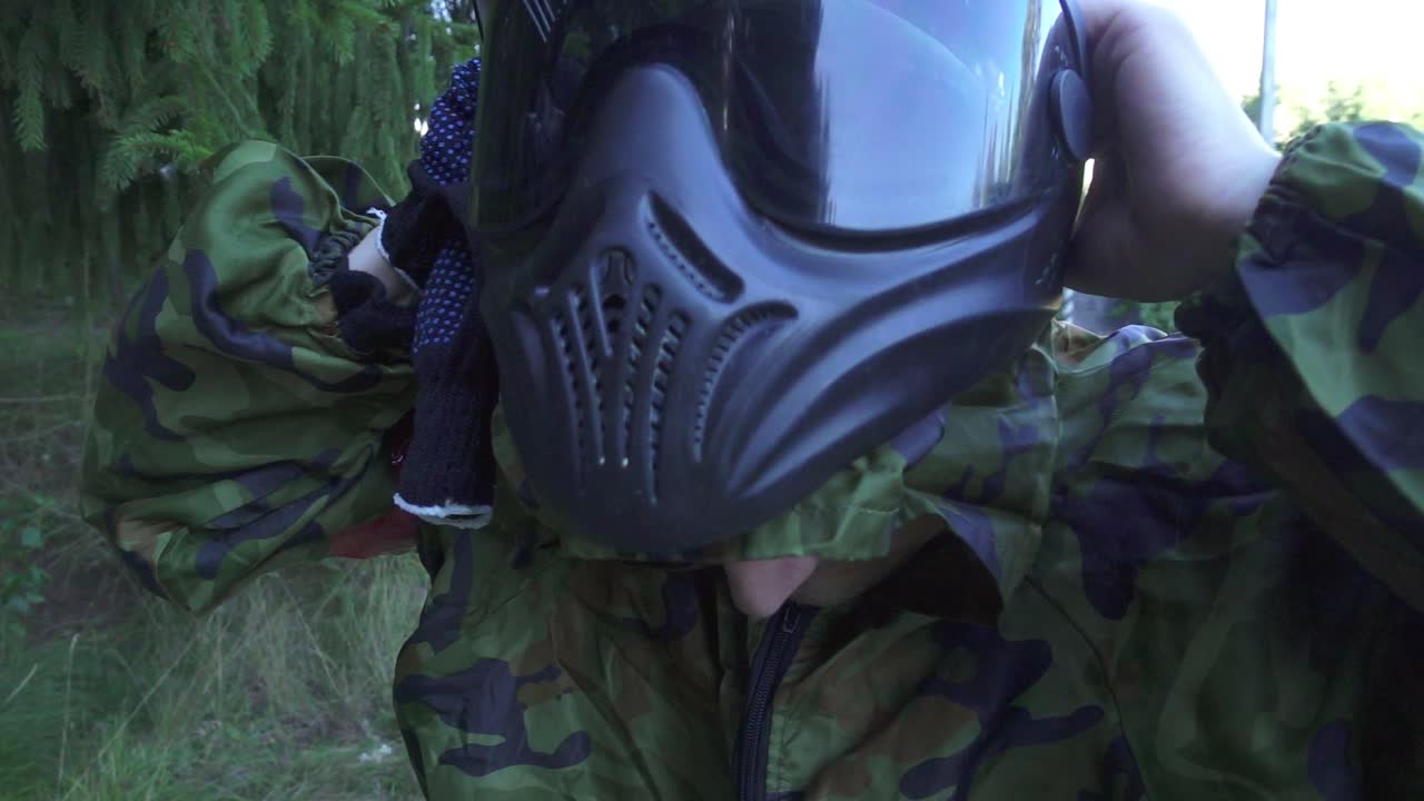 молодой человек надевает пейнтбольную маску на голову перед стрельбой