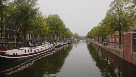 Amplia-Vista-Del-Hermoso-Canal-En-La-Ciudad-De-Amsterdam-Con-Casas-Flotantes-Atracadas-En-El-Muelle