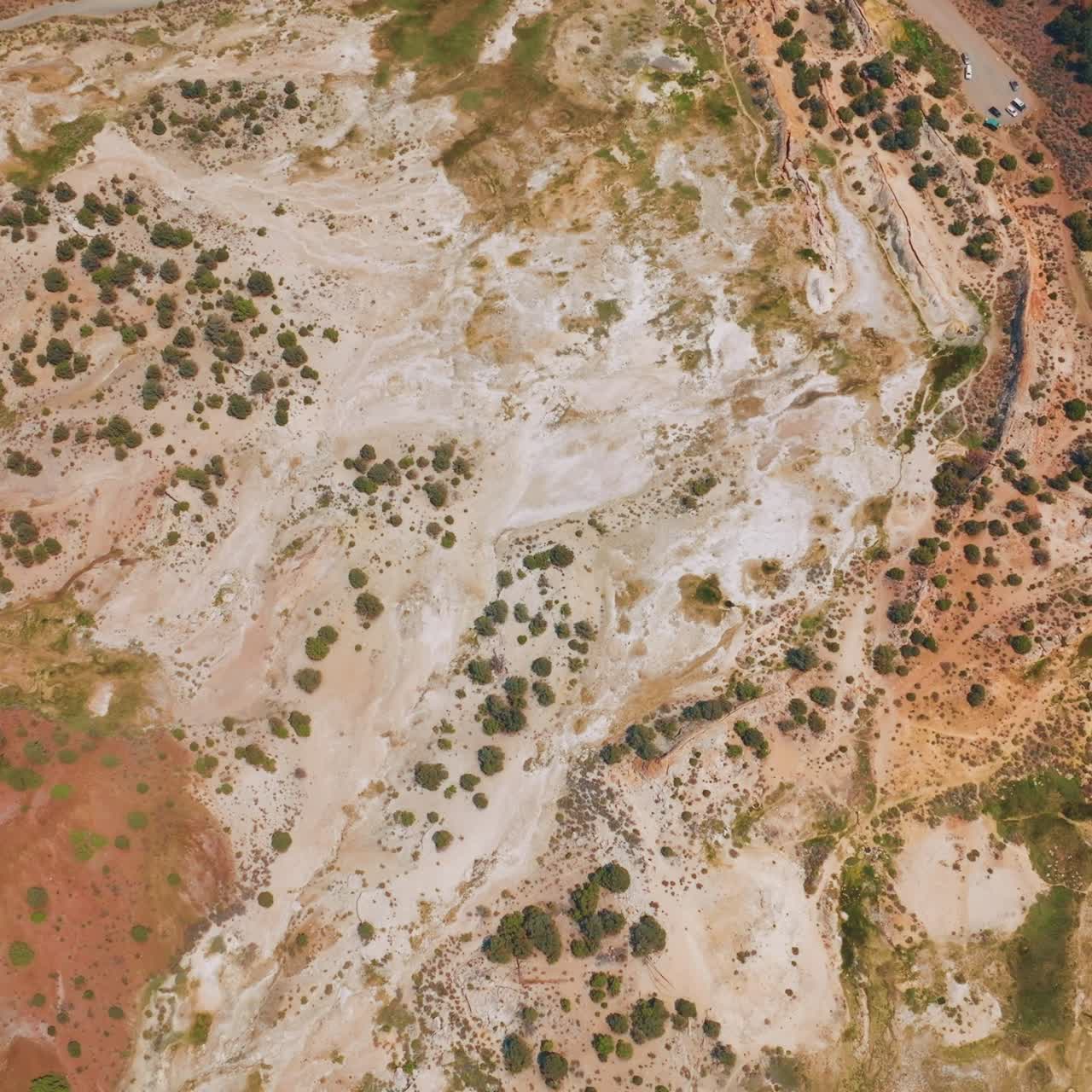Lifeless dry landscape with some bushes growing on. Road with few cars parked. Aerial view of Travertine, California, USA