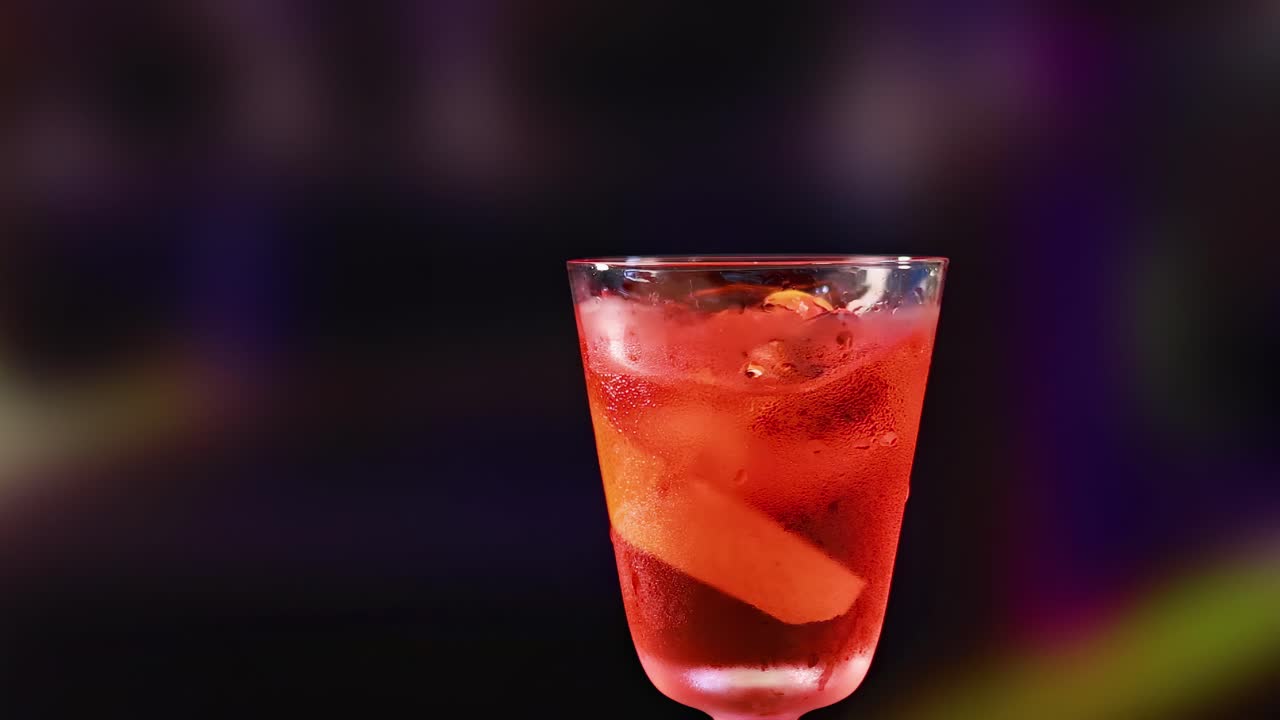 Un primo piano di un cocktail rosso con una scorza d'arancia, su uno sfondo colorato e sfocato.