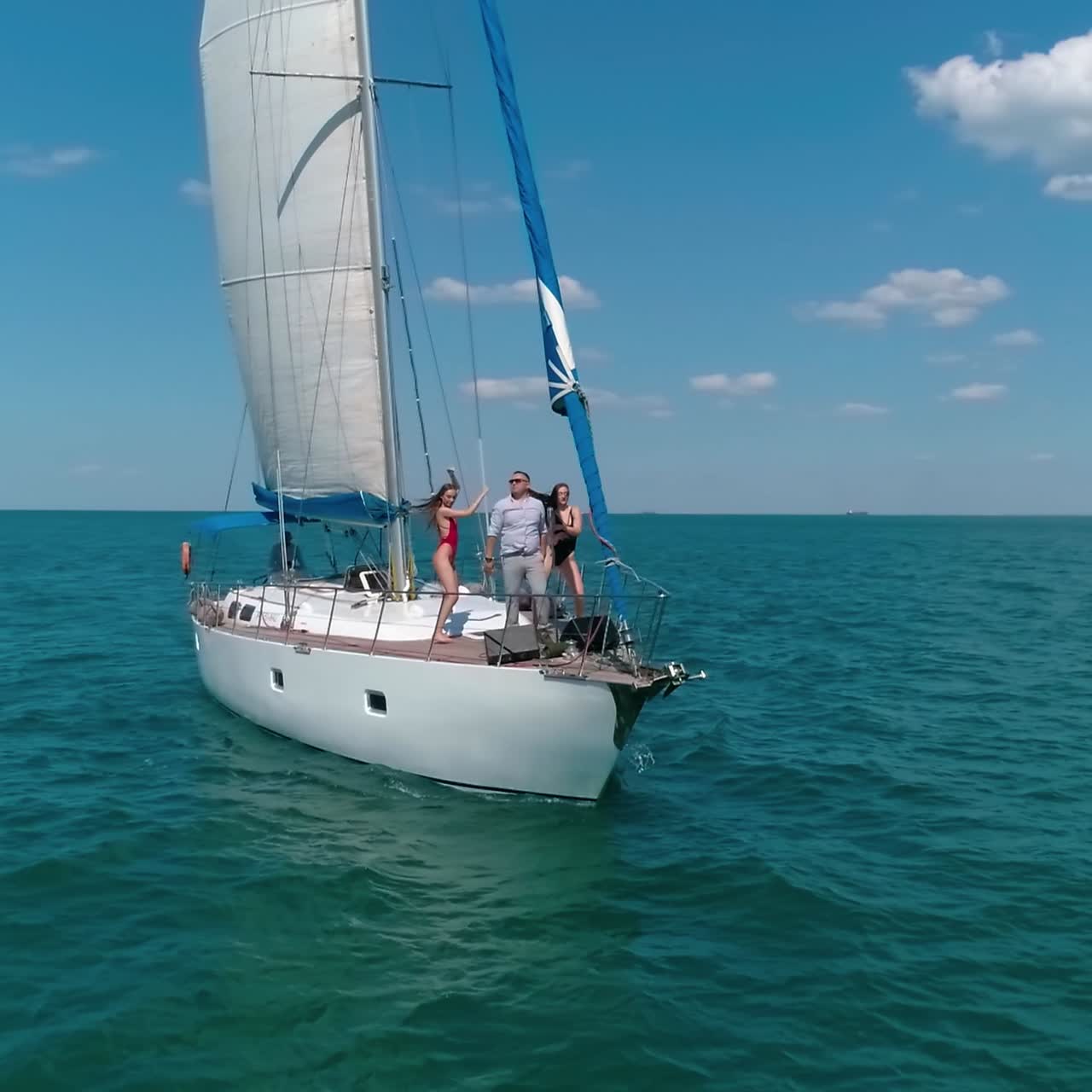 Young people rest on a yacht in summer. Male singer and two girls dancing on a sailboat on blue sea background. Joyful summer sea voyage