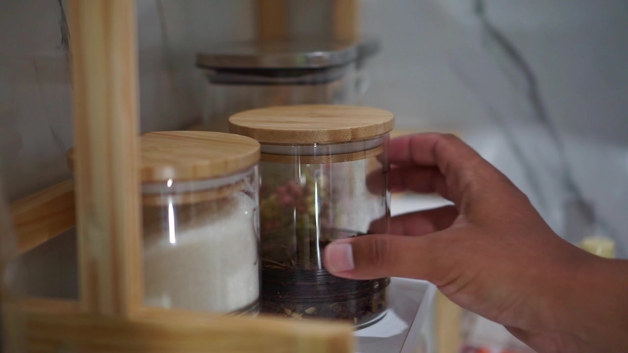 Mano che sistema barattoli di tè su uno scaffale di legno, concetto di organizzazione della cucina e della casa.