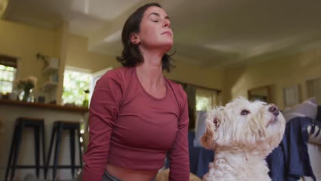 caucasian woman practicing yoga with her pet dog at home