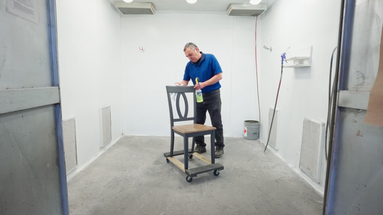 Camera pushes in as worker cleans wooden dining chair with spray and rag