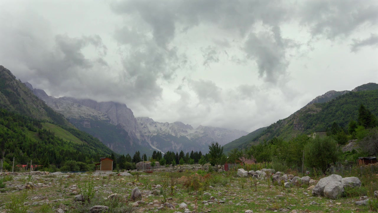 Nuvole tempestose si addensano sulle aspre cime montuose e sui verdi pendii boscosi nel Parco Nazionale della Valle di Valbona, Albania, creando un'atmosfera cupa e drammatica.
