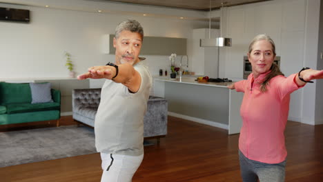 practicing yoga together, multiracial senior couple stretching in living room at home