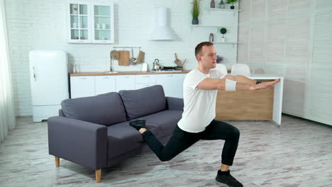 young man exercising at home. guy doing squats with a leg on sofa in the kitchen during isolation at pandemic. sports training in apartment.