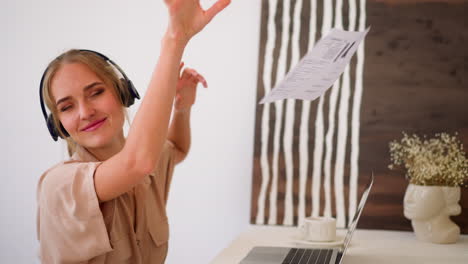 Woman-in-headphones-enjoys-music-throwing-paper-on-laptop