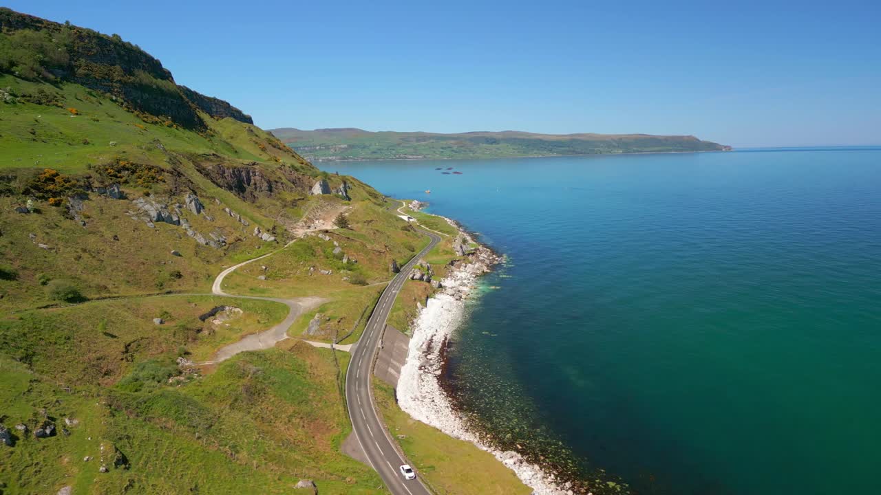 Reversing aerial video of the Causeway Coastal Route at Glenarm in County Antrim, Northern Ireland, UK on a bright and sunny day. Cars pass below. Filmed in 4K, 60FPS and with Rec709 color.