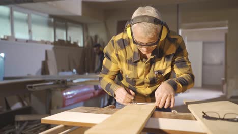 carpintero masculino midiendo madera polvorienta con un medidor y marcando con lápiz.
