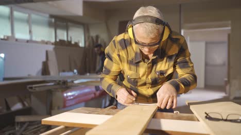 male carpenter measuring dusty wood with meter and marking with pencil.