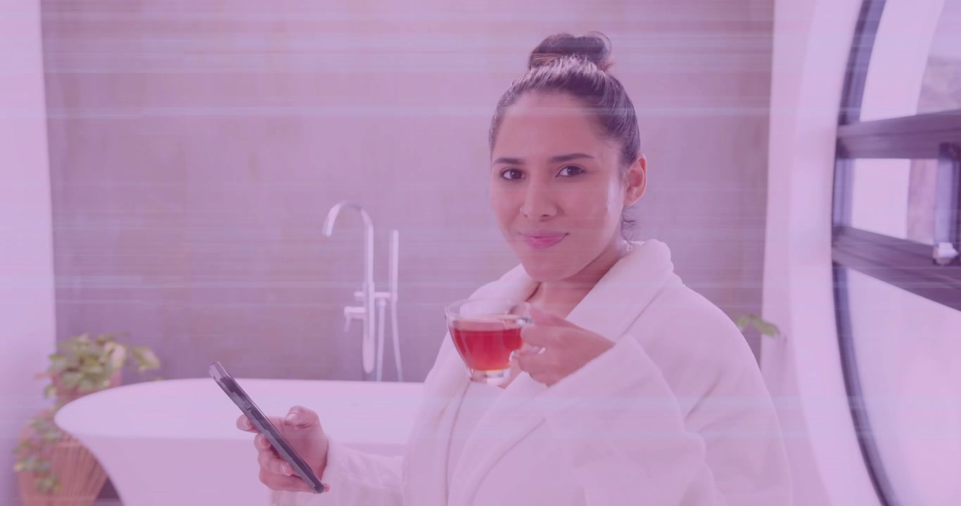 Donna che guarda lo schermo dello smartphone e scorre, sorseggiando tè durante la sua routine di benessere vicino alla vasca.