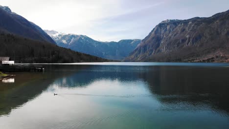 4K-Luftaufnahme-Einer-Brücke-Und-Eines-Bergsees-Dahinter-Mit-Wunderschönen-Schneebedeckten-Klippen