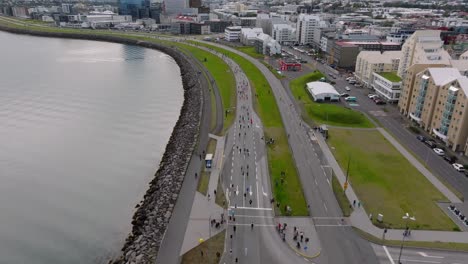 People-running-the-Reykjavik-marathon-in-Iceland-along-sea-shore,-aerial