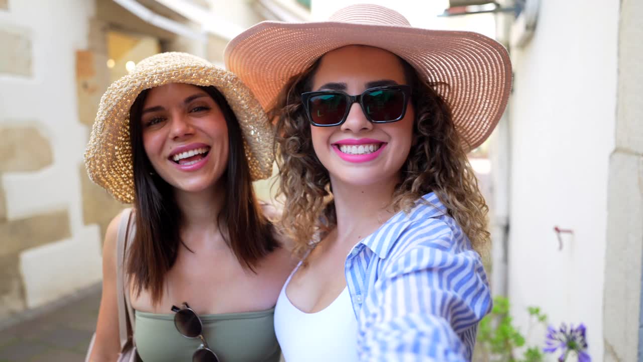 Two women wearing hats and sunglasses are smiling outdoors