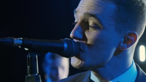 man singing song in microphone during performance on stage on rock concert. close up man rock star singer on music concert on colorful light background