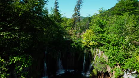 aerial pedestal down in between forest trees to reveal cascading waterfalls at plitvice lakes, croatia