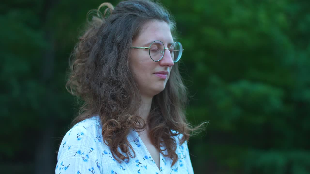 una mujer joven al aire libre, con gafas meditando con los ojos cerrados