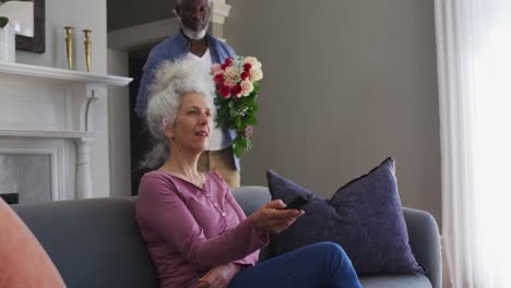 hombre mayor afroamericano dando un ramo de flores a su esposa en casa