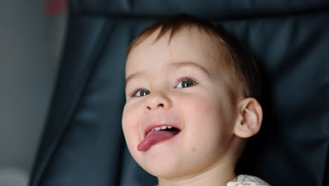 funny playful baby boy sits in office chair. cute kid shows tongue to camera. close up.
