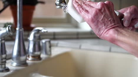 Close-up-on-the-hands-of-an-old-woman-cleaning-and-polishing-a-vintage-silverware-handle-in-the-sink-to-remove-tarnish-and-make-it-shiny