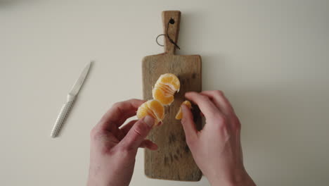 Peeling-and-tearing-a-Tangerine-with-hands-in-kitchen-4K-Top-Shot-POV