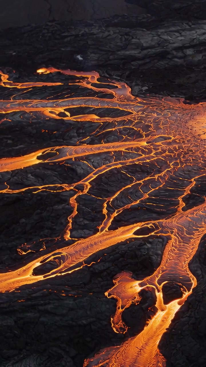 Video verticale: Lava fusa che scorre e si ramifica su una pianura basaltica da un condotto, formando pozze incandescenti.