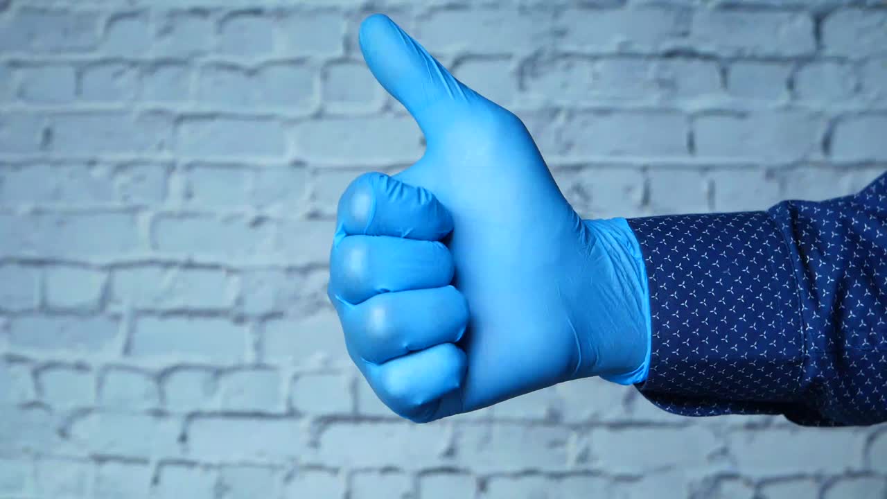 파란색 니트릴 장갑을 입은 손으로 엄지손가락을 들어 올립니다.