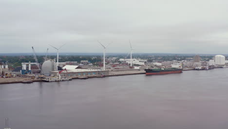 cargo ship docked at the port with wind turbines on a cloudy day