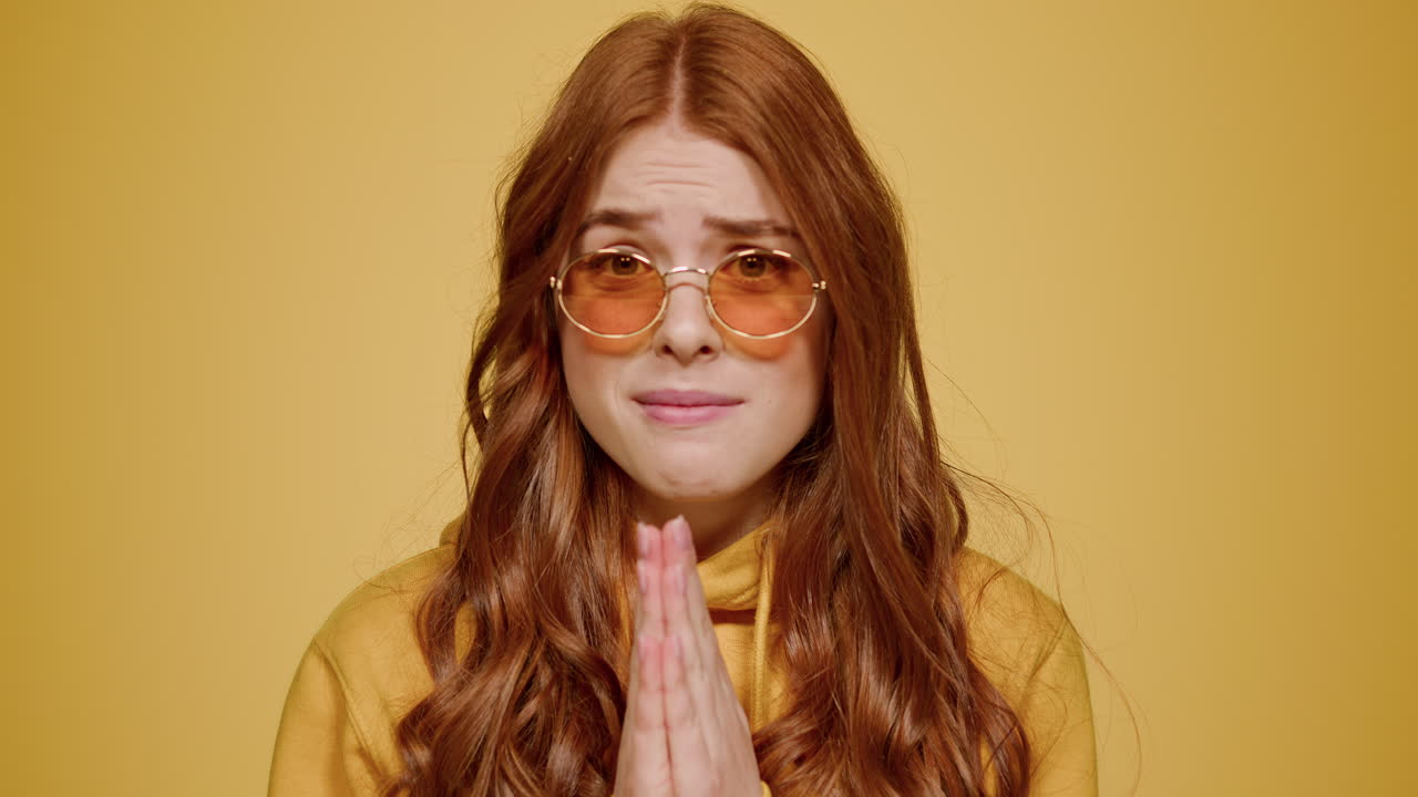 Upset girl making praying gestures in studio. Confused woman begging indoors
