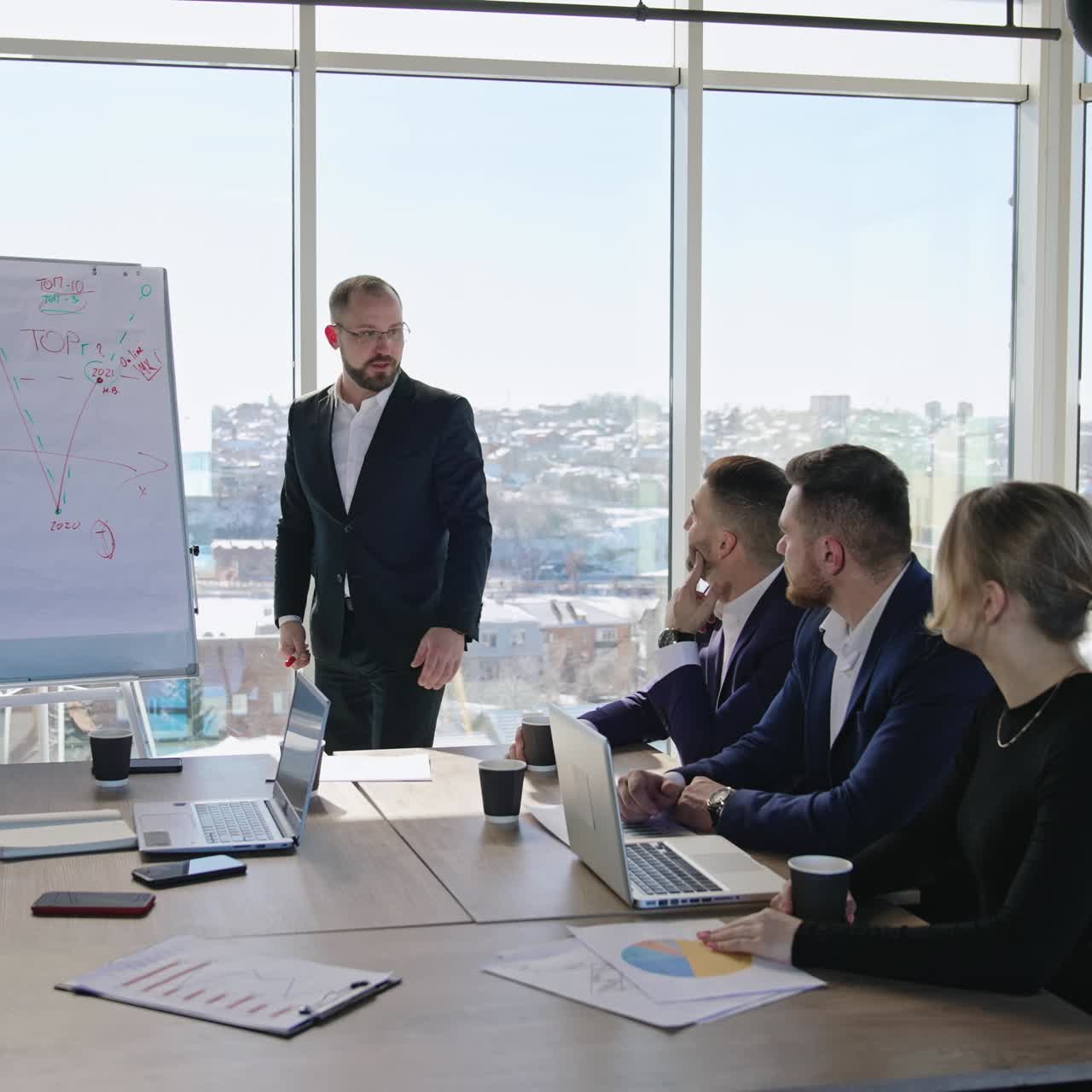 Group of business people having meeting in office with big windows. Presenter discussing the chart emotionally and gesturing energetically. Team listening to their colleague attentively