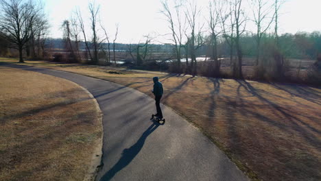 an aerial tracking of a man on an electric skateboard in an empty park on a sunny day