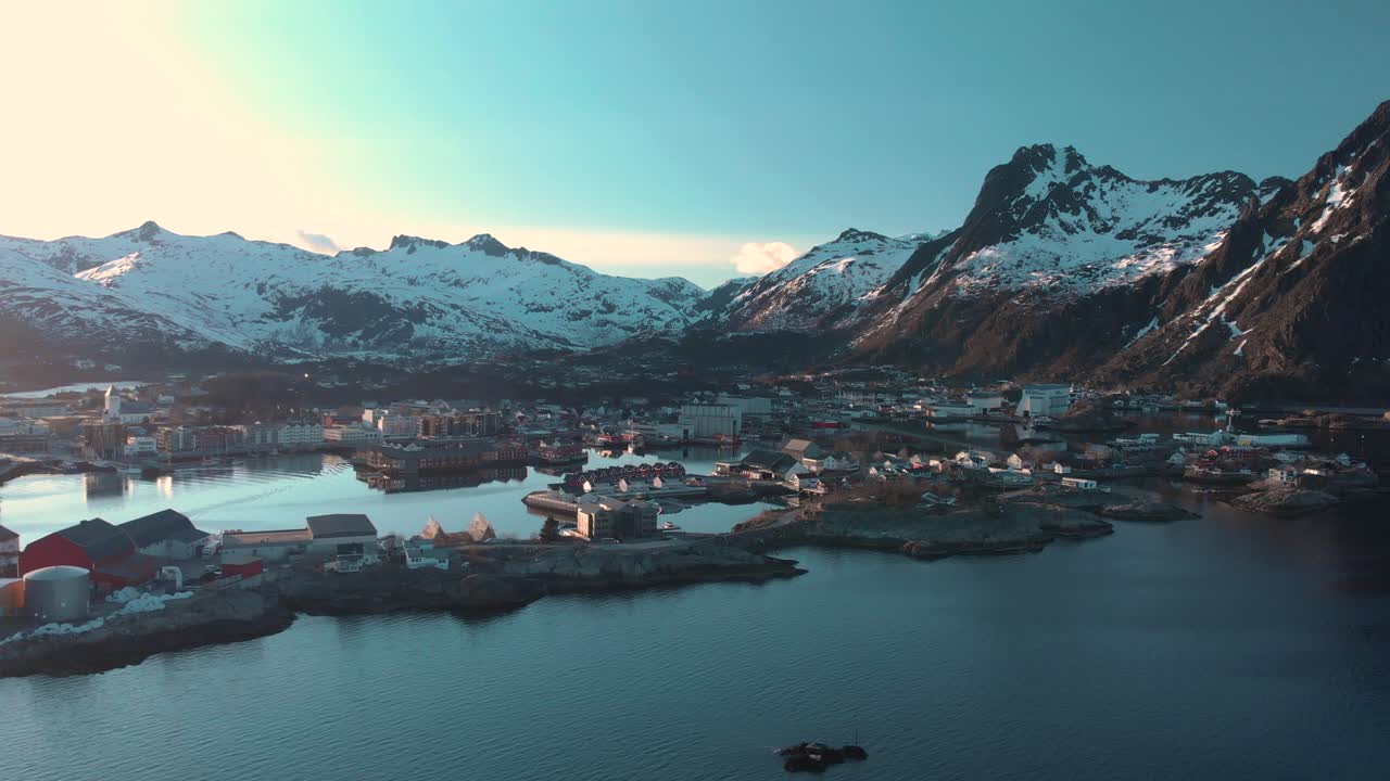 Aerial drone shot of the blue ocean in Lofoten, Norway and a small village and mountains in the background.