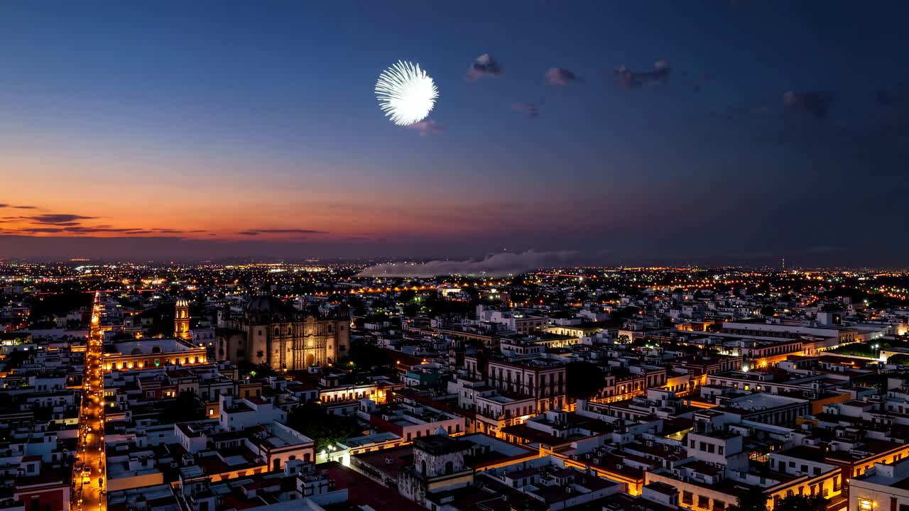 Aerial video captures vibrant fireworks exploding over a cityscape at dusk, showcasing a festive