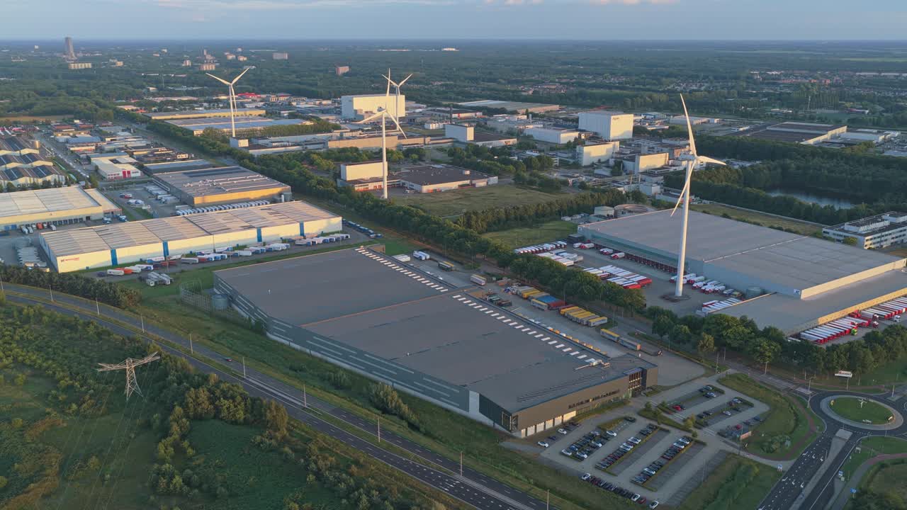 Sunset aerial of warehouses with solar rooftops beside wind turbines, Holland