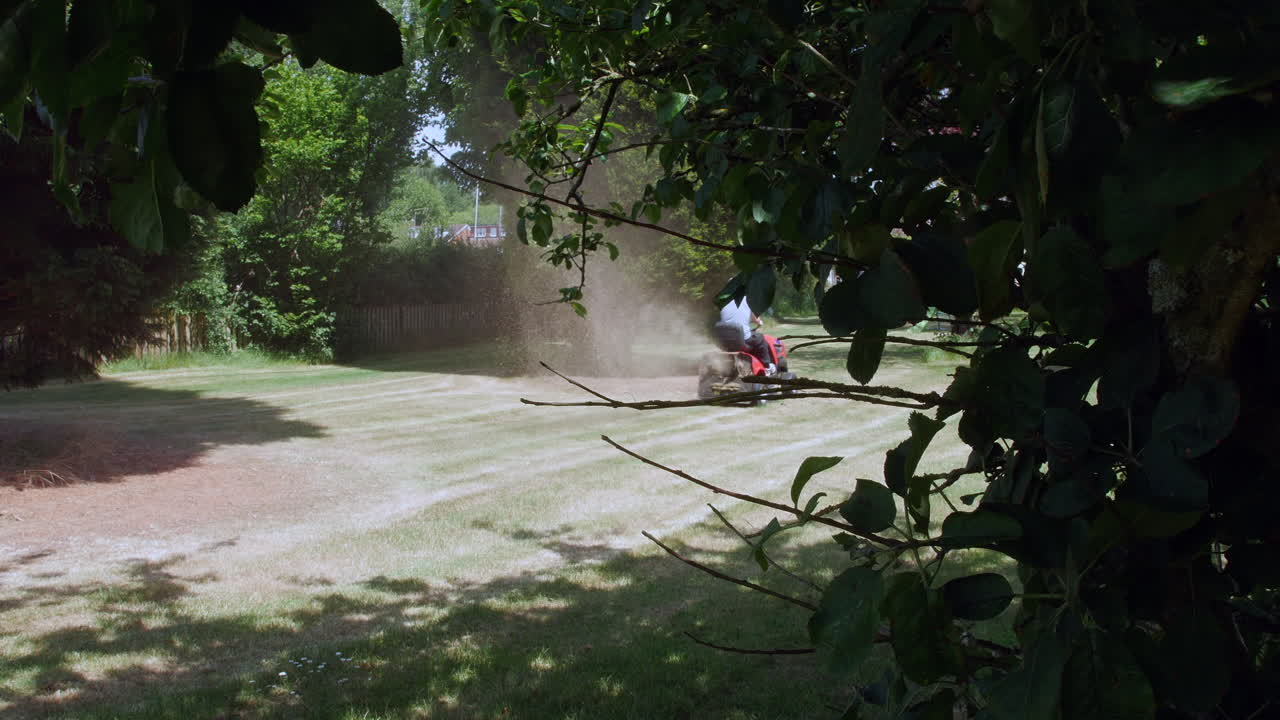 мужчина рассыпает скошенную траву во время стрижки газона с помощью сидячей газонокосилки летом