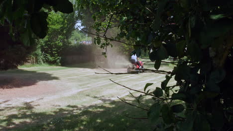 a man spraying grass cuttings while mowing the grass using a sit down ride on lawn mower in summer