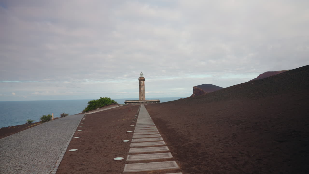 Telecamera che si muove verso il Faro di Ponta dos Capelinhos nelle isole vulcaniche portoghesi di Faial nelle Azzorre, Oceano Atlantico settentrionale, Portogallo.