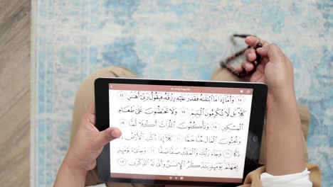 reading quran scripture from ipad holding prayer beads, islamic dhikr