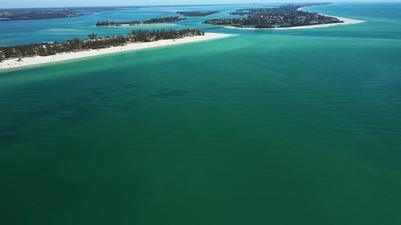 Calm turquoise waters surround the sandy shoreline of Bradenton Beach, creating a tranquil coastal scene.