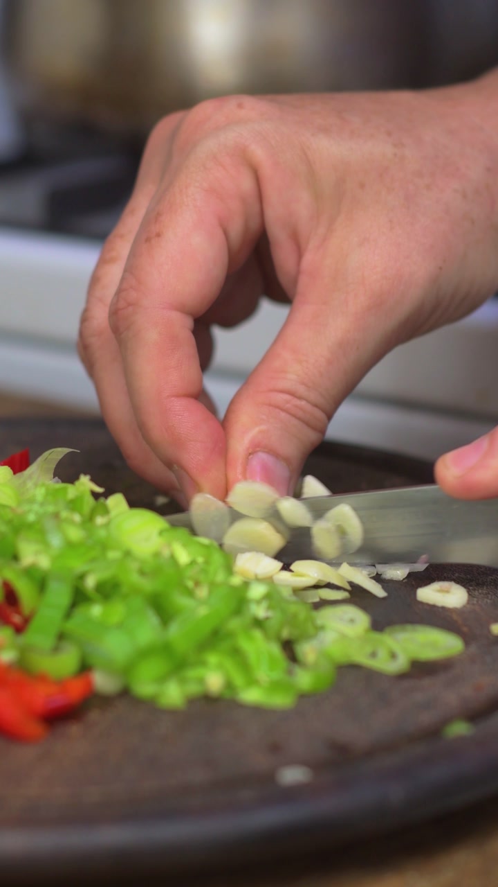 Close up of hands slicing garlic for home cooked meal on wooden surface in kitchen